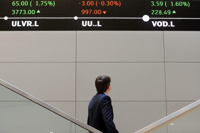 <p>A man looks up at electronic ticker tape showing the FTSE 100 inside the London Stock Exchange</p>