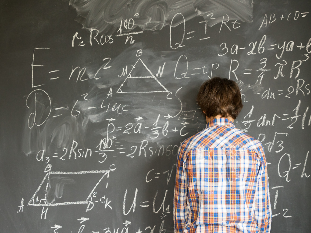 Person leaning their head against a blackboard covered in equations