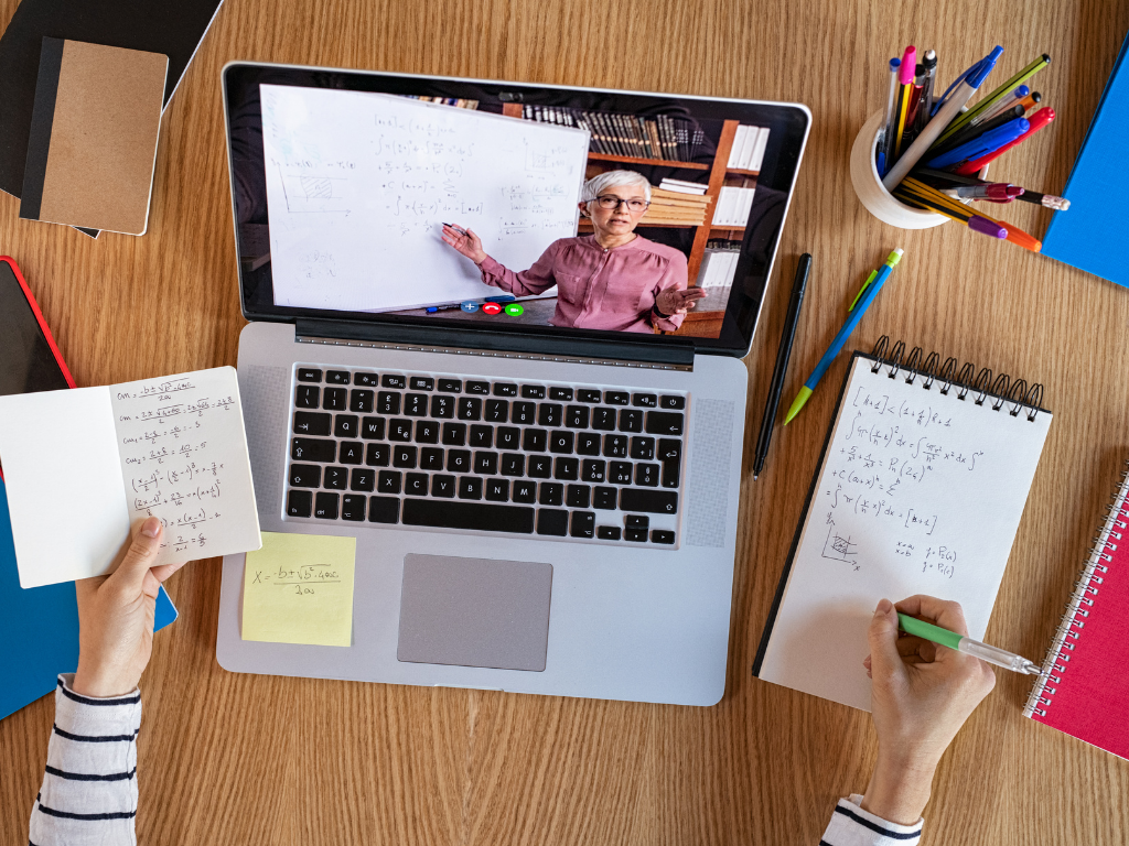 Educational video playing on a laptop, surrounded by notes on a desk